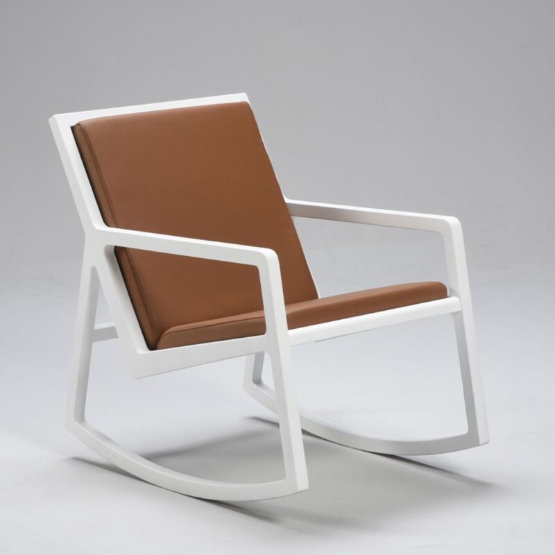 Lux keinutuoli, runko valkoinen, istuin- ja selkäosa pehmustettu ja verhoiltu ruskealla nahalla.